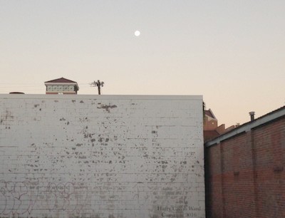 A white wall with the moon setting in the distance